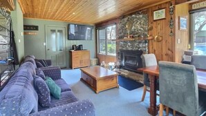 A cozy living room with a stone fireplace, wooden ceiling, and a television mounted on the wall. - Glacier Chalet (Dinner Plain)