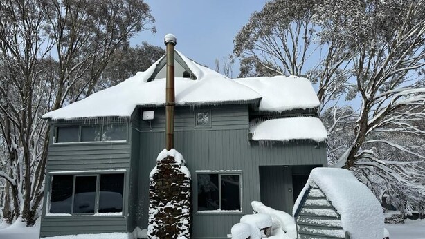 A two-story house with a snow-covered roof and surrounding trees. - Glacier Chalet (Dinner Plain)
