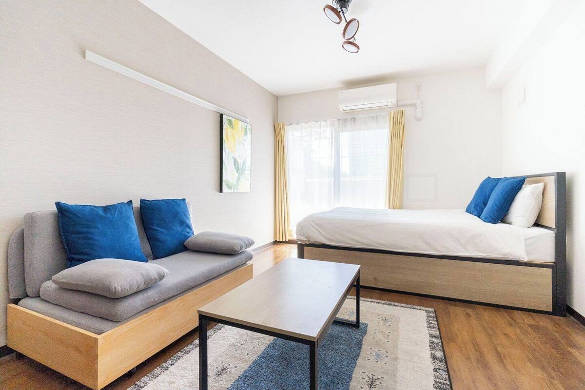 Una habitación moderna con sofá, cama, mesa y ventana con cortinas.