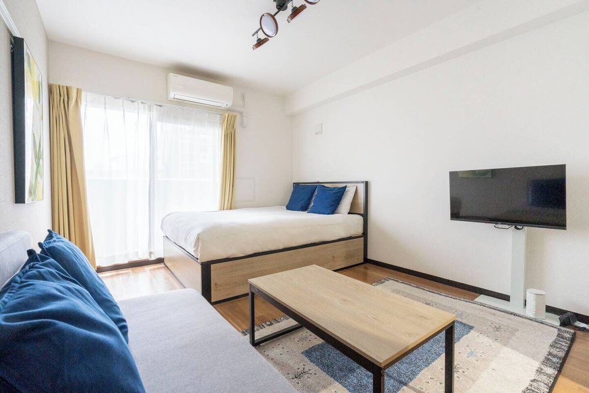 Una habitación de hotel moderna con una cama, televisor, sofá y una pequeña mesa.