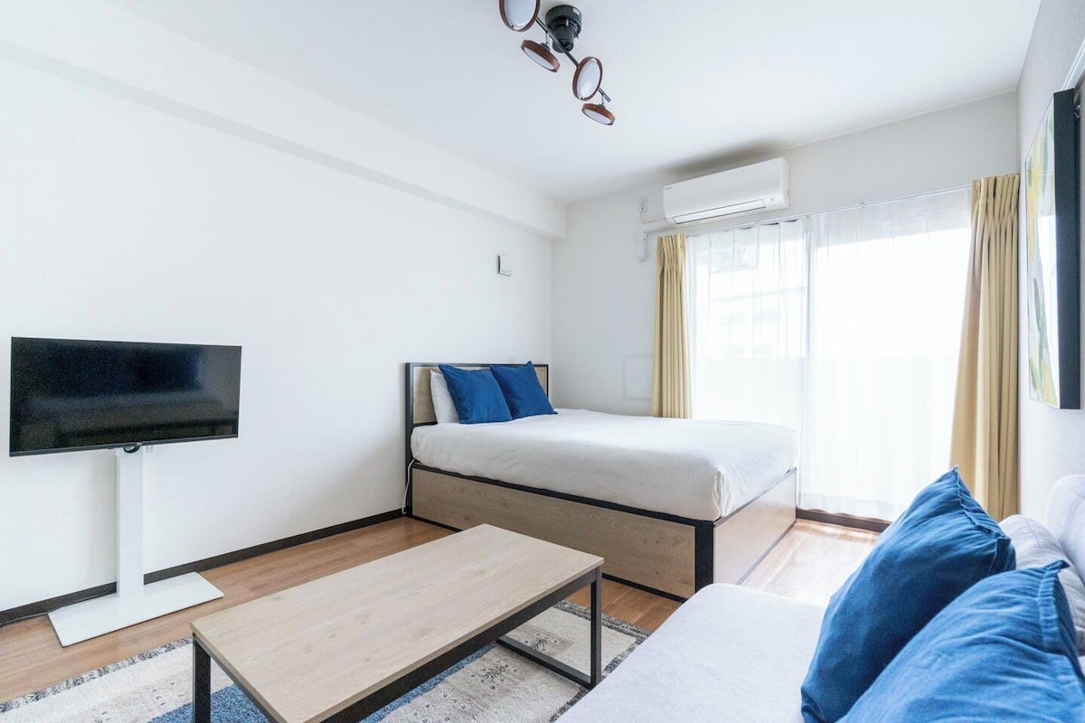 Una habitación de hotel con una cama, televisión, sofá, mesa de centro y aire acondicionado.