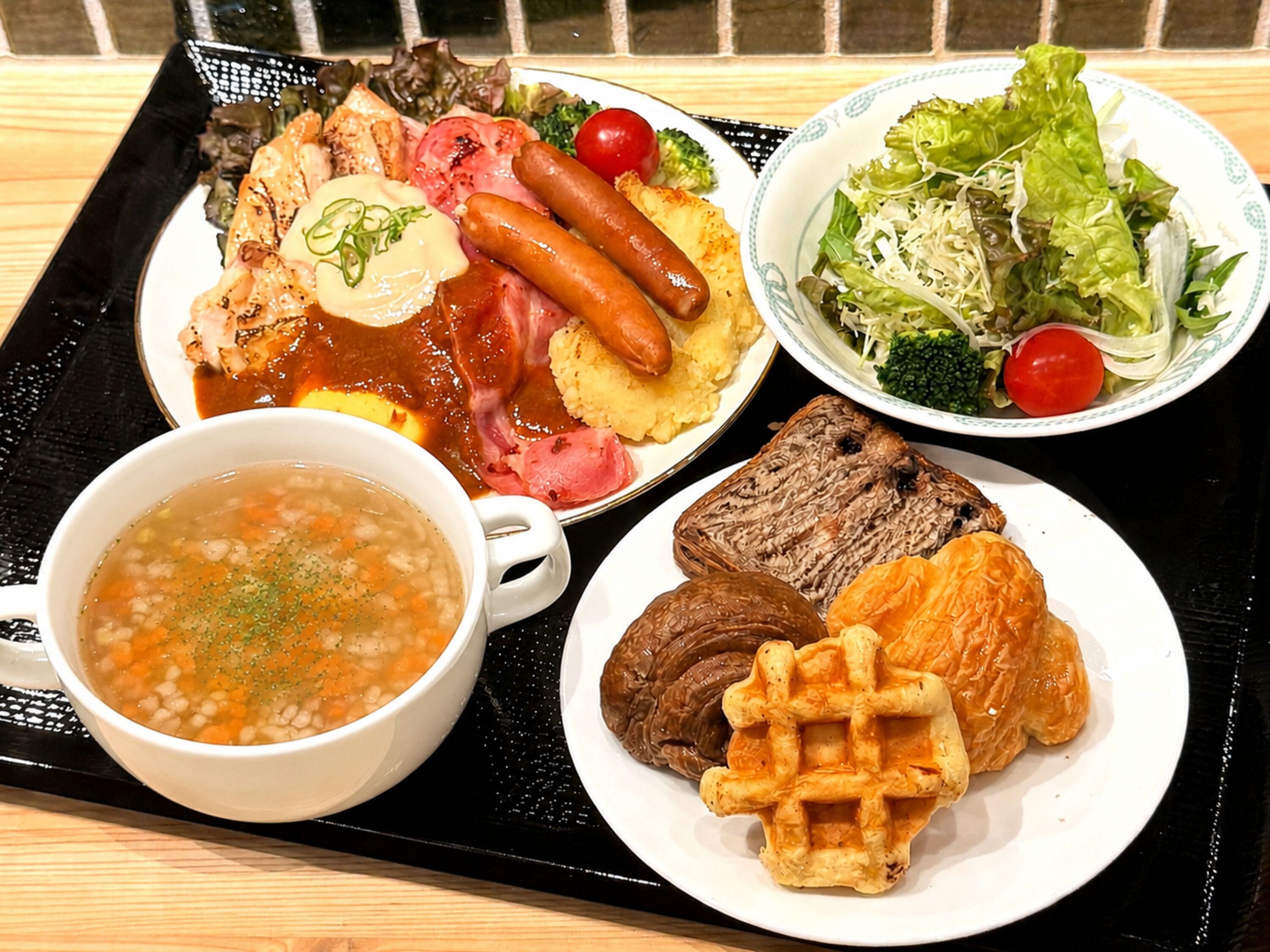Una bandeja con una variedad de platillos, incluyendo un tazón de sopa, un plato con salchichas, un bistec y una ensalada.