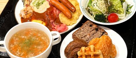 Una bandeja con una variedad de platillos, incluyendo un tazón de sopa, un plato con salchichas, un bistec y una ensalada.