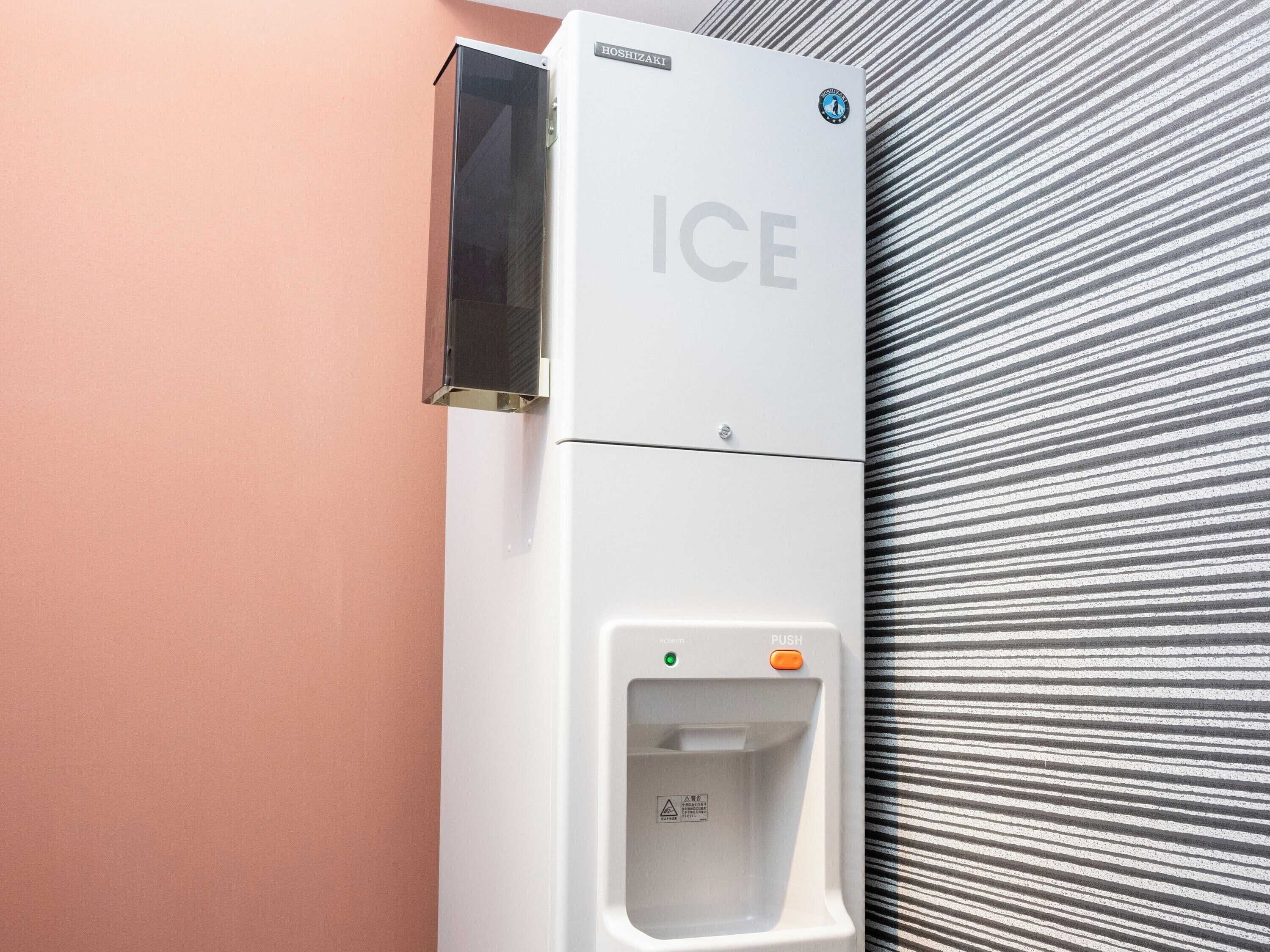 A white ice dispenser with a push button and a power indicator on a wall.