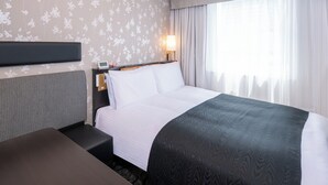 Une chambre d’hôtel avec un lit, une table de chevet, une lampe et une fenêtre avec des rideaux.