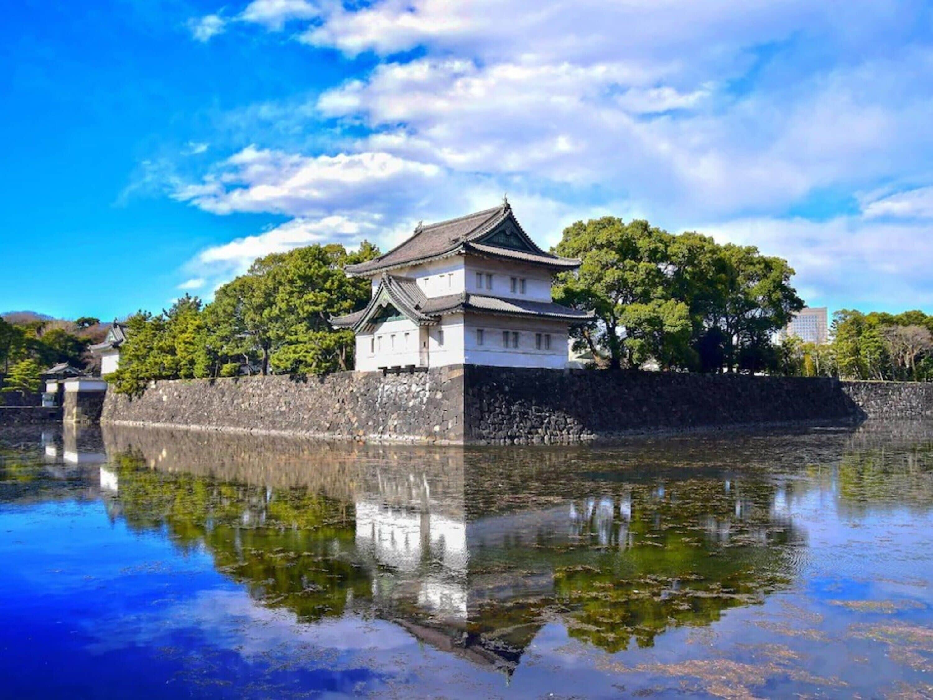 A traditional Japanese castle with a reflection in the water, surrounded by trees and a clear sky.