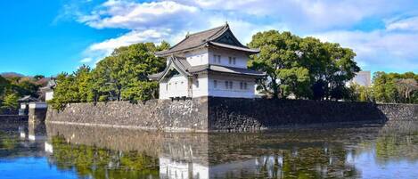 A traditional Japanese castle with a reflection in the water, surrounded by trees and a clear sky.