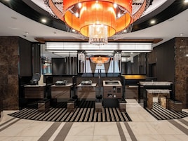 A modern lobby with a large chandelier, a reception desk, and a check-in counter.