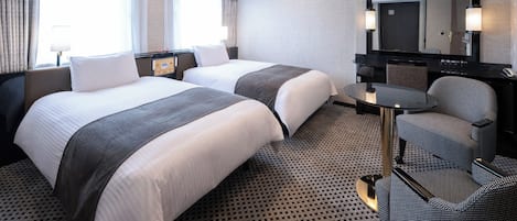 A hotel room with two beds, a desk, a chair, a mirror, and a ceiling light.