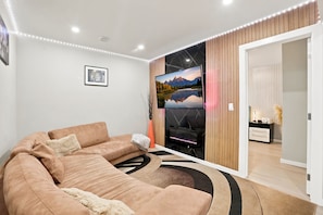 A modern living room with a large flat-screen TV, a beige sofa, and a wooden accent wall. - Cozy 1-Bedroom Apartment in Calgary with Kitchenette (Calgary)
