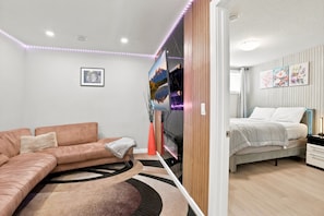 A modern bedroom with a bed, a sofa, a TV, and artwork on the walls. - Cozy 1-Bedroom Apartment in Calgary with Kitchenette (Calgary)