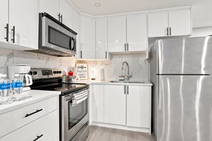 A modern kitchen with white cabinets, stainless steel appliances, and a coffee maker. - Cozy 1-Bedroom Apartment in Calgary with Kitchenette (Calgary)