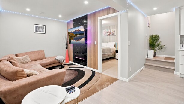 Uma sala de estar moderna com sofá, mesa de centro e televisão. Uma escada leva a outro cômodo.