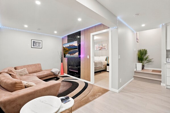A modern living room with a sofa, a coffee table, and a TV. There is a staircase leading to another room.