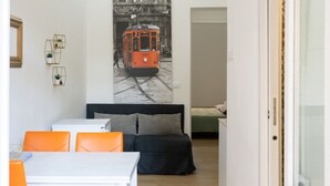 Una habitación funcional con cama, una mesa de comedor con sillas, una estantería en la pared con plantas y un cartel grande de un tranvía.