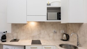 Una cocina moderna con armarios blancos, microondas integrado, hervidor y cafetera.