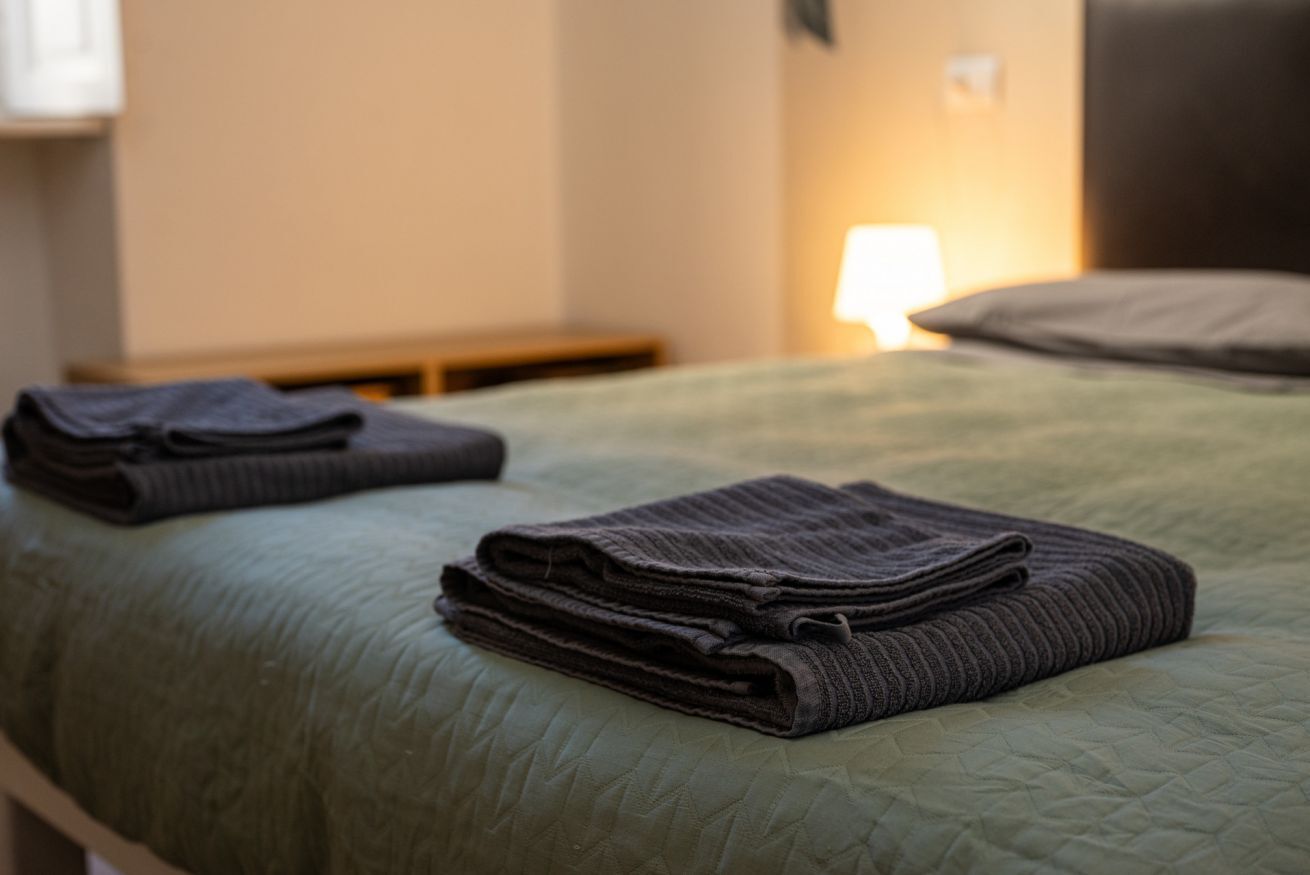 A neatly made bed with a green quilt and folded dark towels.