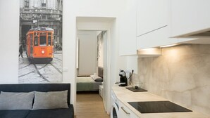 Una habitación compacta con cama, kitchenette, lavadora y estante empotrado.