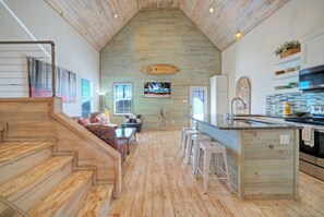 A spacious kitchen with wooden floors, a central island, bar stools, and a view of the beach through a window. - 3 Laguna Madre Homes • Pool + Bay Access | Sleeps 21 | Laguna Village Collection (Corpus Christi)