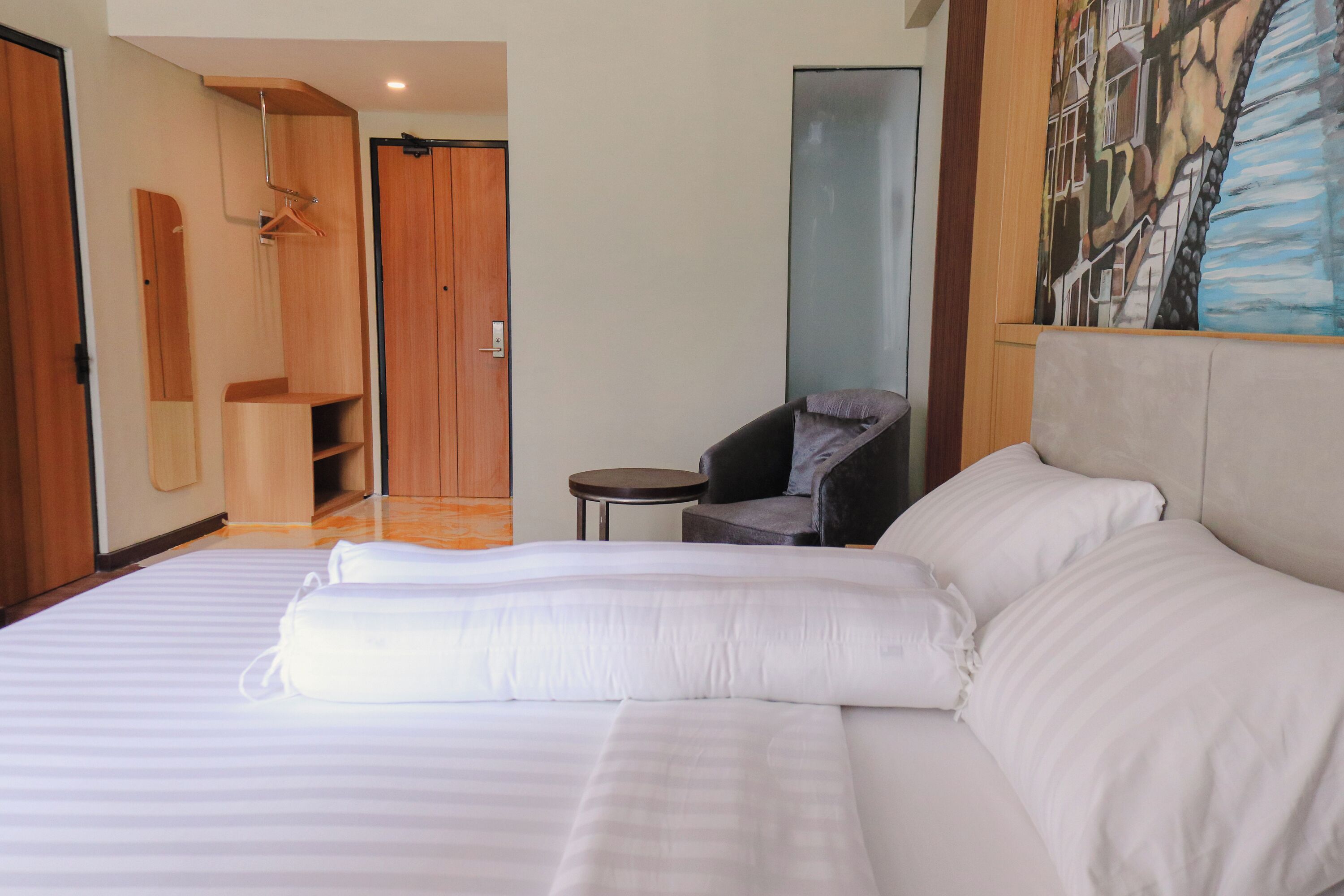A hotel room with a large bed, a chair, a small table, a wardrobe, and a painting on the wall.
