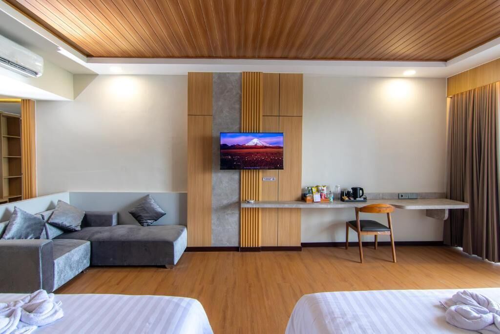Una habitación de hotel moderna con techo de madera, un televisor de pantalla plana en la pared, un sofá, un escritorio con silla y dos camas.