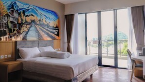 A hotel room with a bed, a desk, a chair, a painting on the wall, and a view through the window. - Azana BeSt Hotel Batu (Batu)