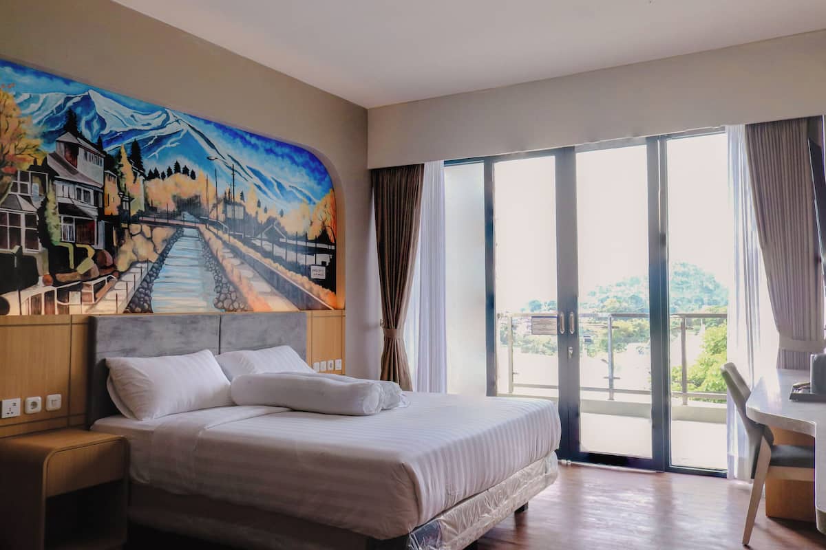 Habitación de hotel con cama, escritorio, silla, un cuadro en la pared y vistas por la ventana.