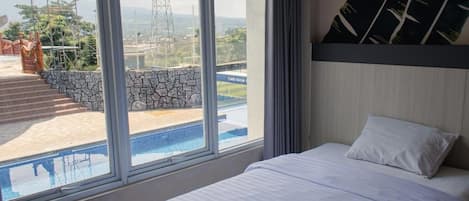 Habitación de hotel con cama, ventana grande y vistas a una piscina y una obra en construcción.