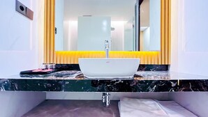 A bathroom with a white sink, a mirror, and a yellow accent wall. - Azana BeSt Hotel Batu (Batu)