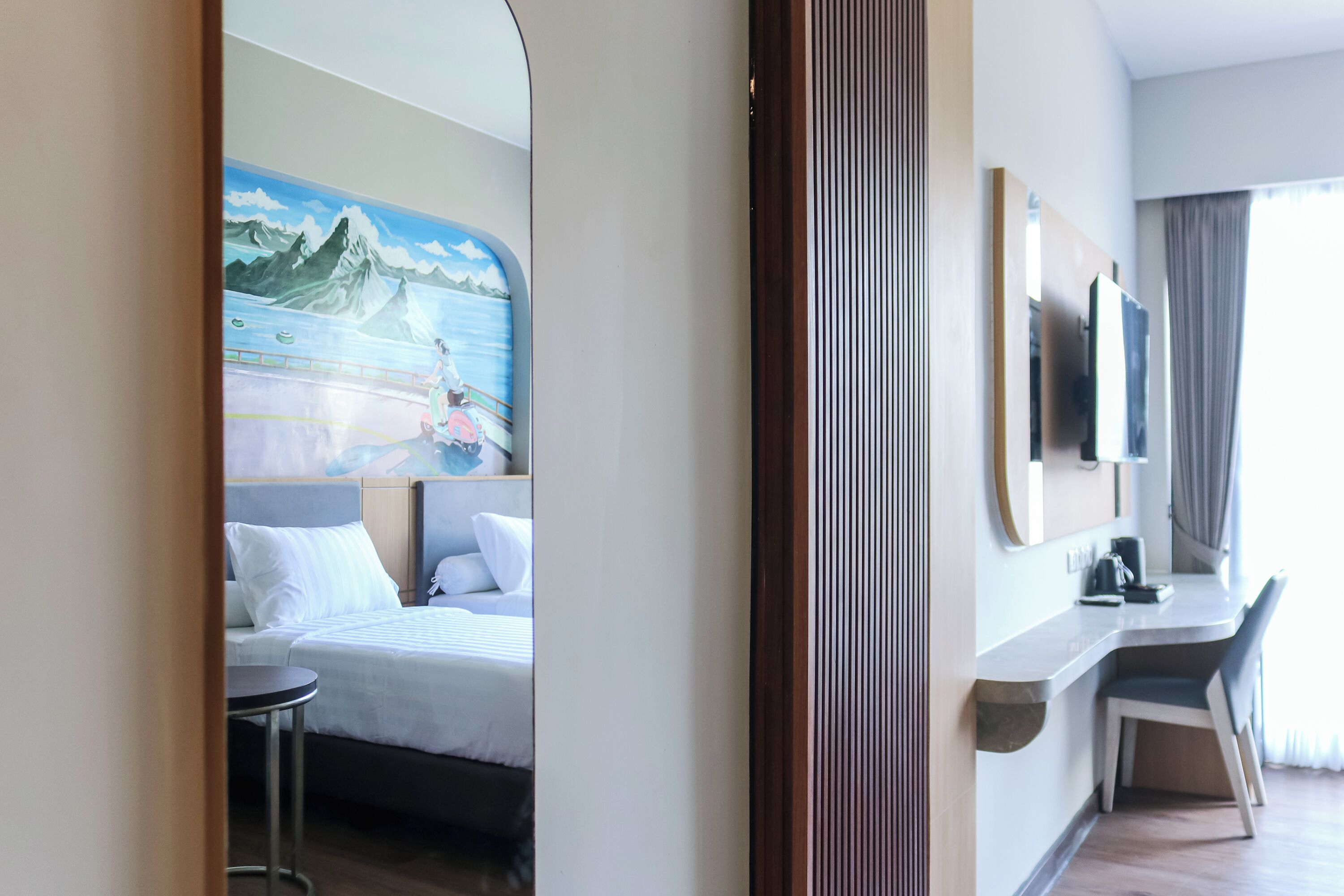 Habitación de hotel con cama, escritorio, silla, televisor y un cuadro de un paisaje montañoso.