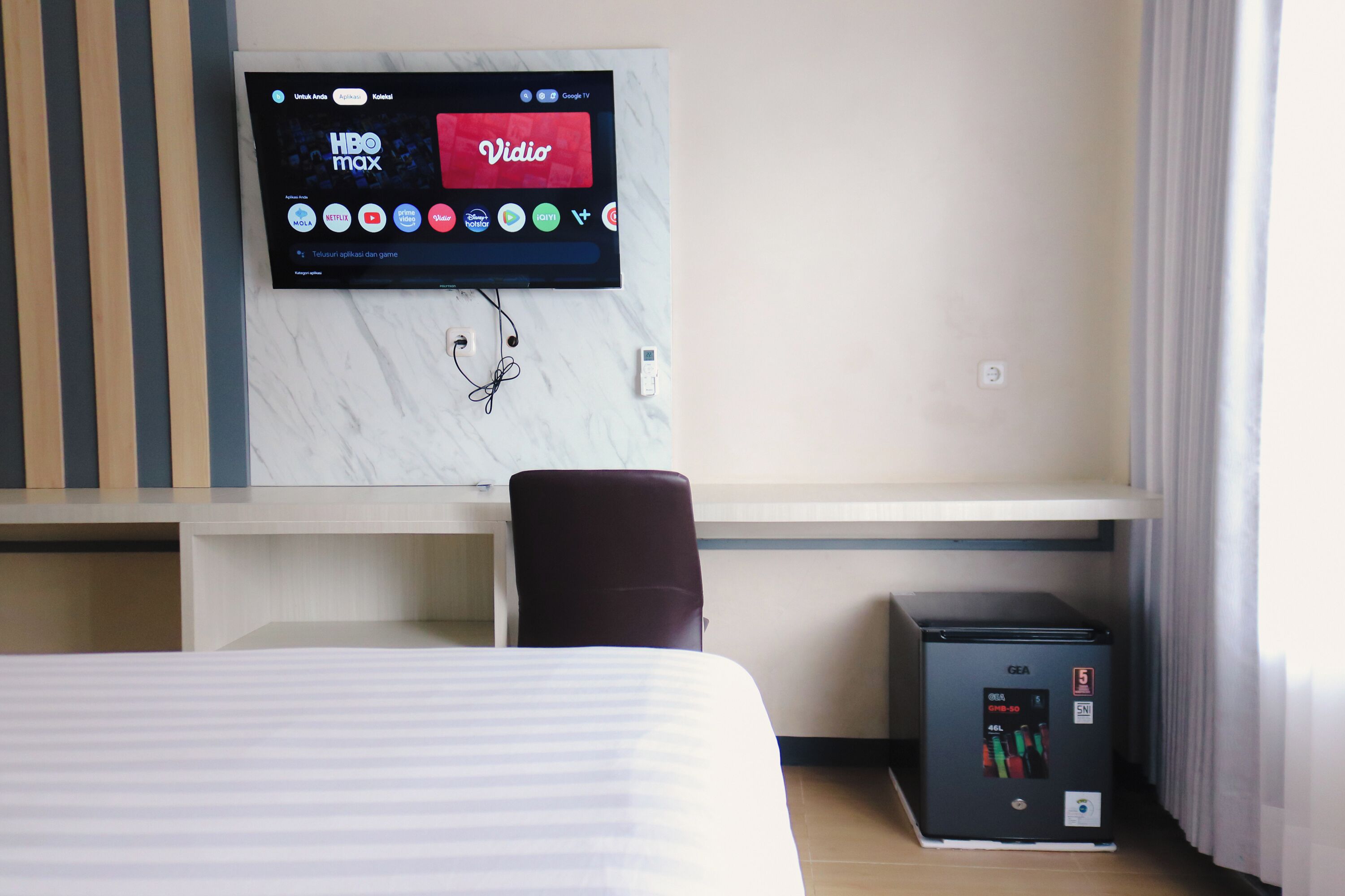 Ein Hotelzimmer mit Bett, Schreibtisch, Stuhl, Wand-Fernseher und Minibar.