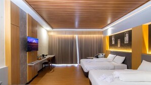 A hotel room with a wooden ceiling, a flat-screen TV, two beds, a desk, and a seating area. - Azana BeSt Hotel Batu (Batu)