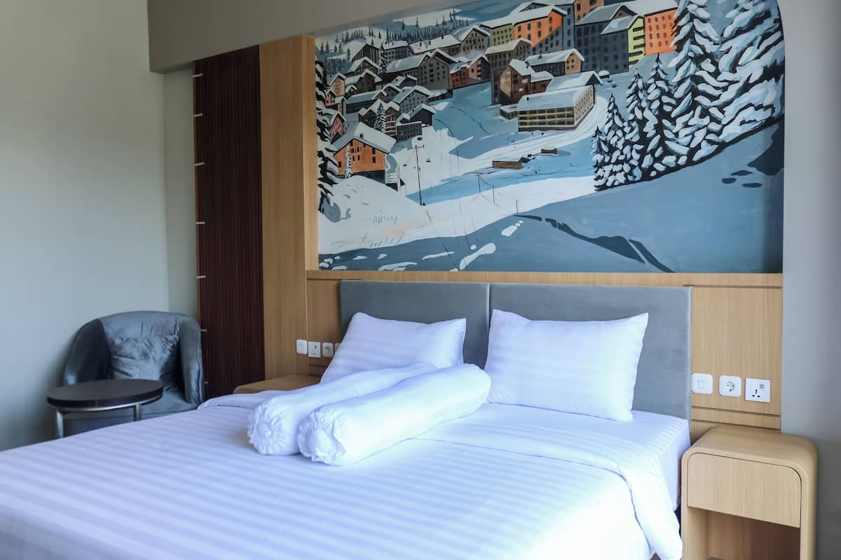 Una habitación de hotel con cama, una silla, un cuadro de un pueblo nevado y un cabecero de madera.
