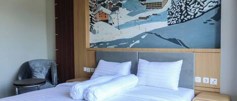 Ein Hotelzimmer mit einem Bett, einem Sessel, einem Gemälde einer verschneiten Ortschaft und einem hölzernen Kopfteil.