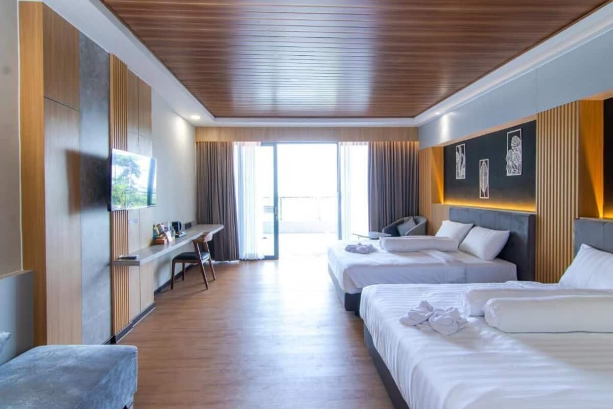 Habitación de hotel con dos camas, un escritorio, televisor y vistas al exterior.