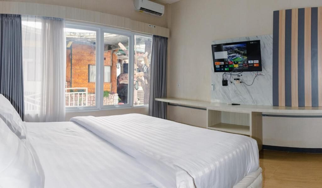 A hotel room with a bed, a TV mounted on the wall, a window with curtains, and a view of the outside.