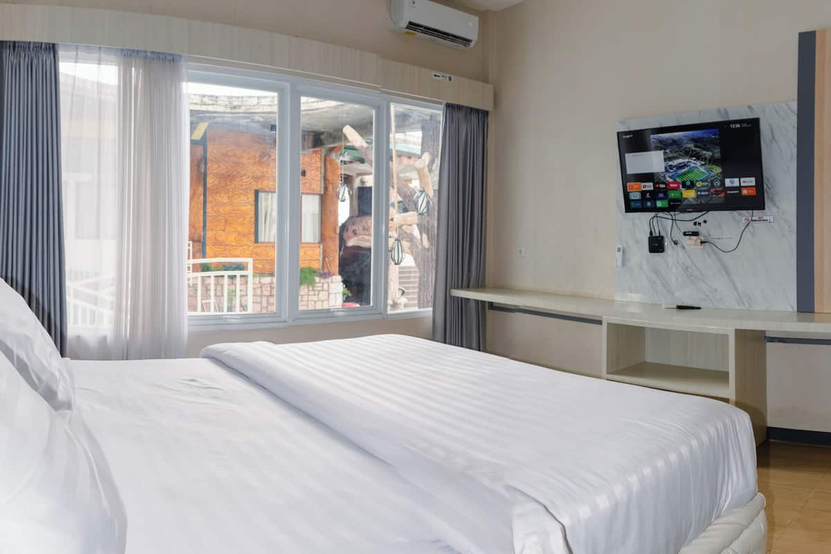Una habitación de hotel con una cama, un televisor montado en la pared y un ventanal con cortinas.