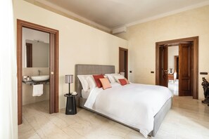 A bedroom with a large bed, a bedside table, a nightstand, a bathroom with a sink, and a mirror. - Elegant Historic Home with Direct View of Piazza Venezia - Capitol House (Roma)
