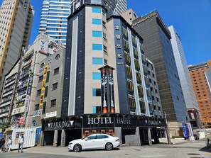 A hotel with a prominent sign for 'HOTEL HAUTE' and a parking area in front. - Ocean View Haute Hotel (Busan)