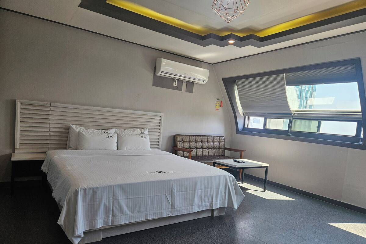 A modern bedroom with a large bed, a sofa, a small table, and a skylight.