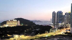 Paisagem urbana com arranha-céus, uma colina com um edifício no topo e um corpo d'água ao fundo.