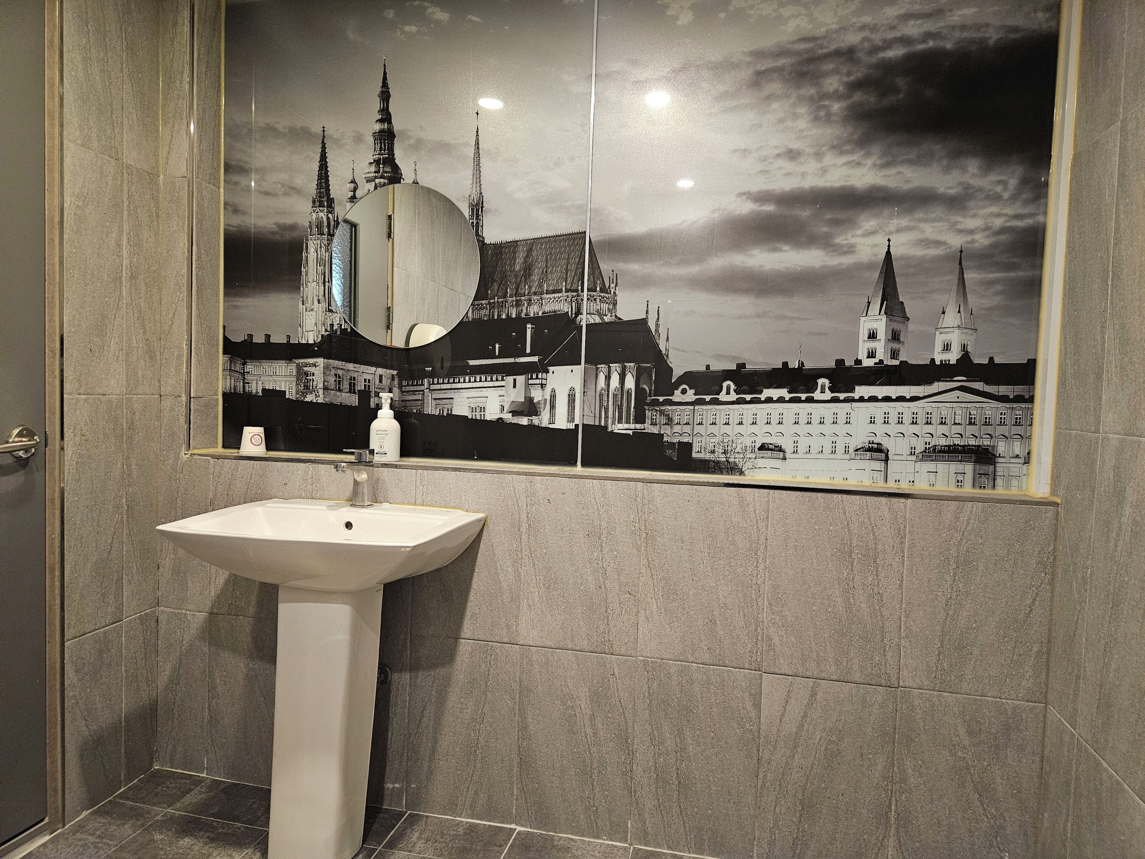 Un baño con un espejo grande que refleja un paisaje urbano, un lavabo y una puerta.