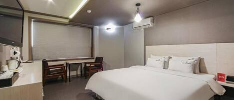 Quarto de hotel com cama, escrivaninha, cadeiras e ar condicionado.