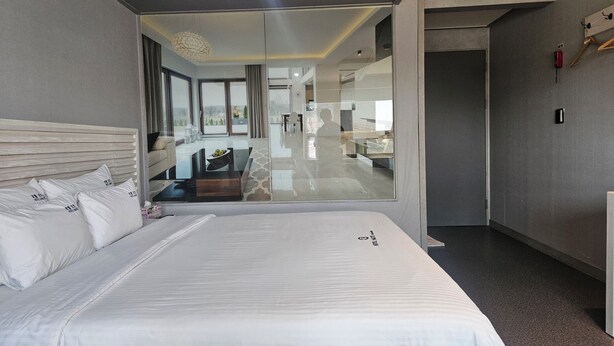 Quarto de hotel moderno com uma cama grande, parede de vidro e vista para a área de refeições.