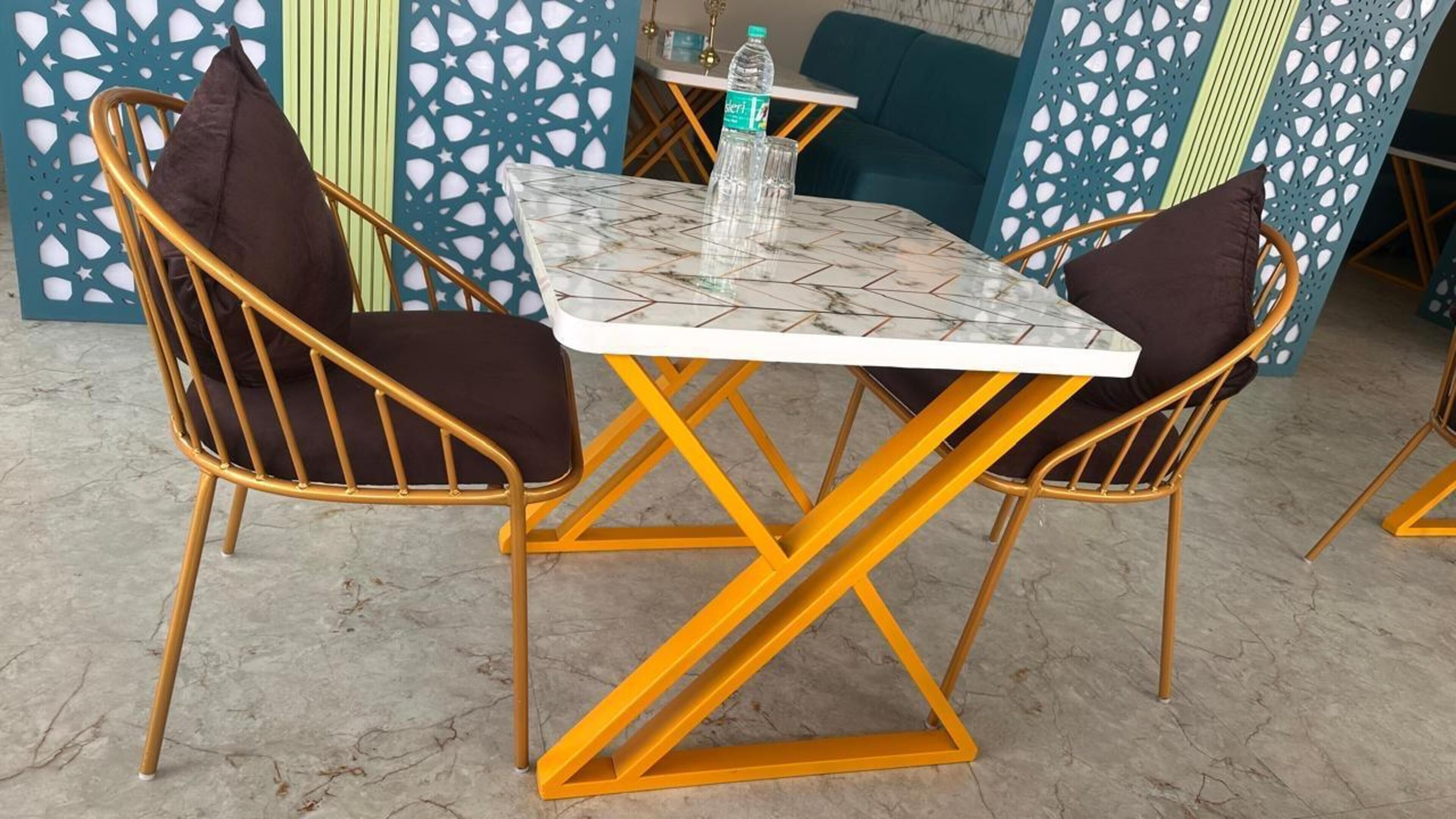 Un coin repas avec une table et des chaises, une bouteille d’eau et un mur décoré de motifs.