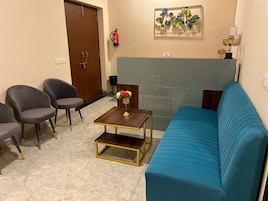 Uma sala de estar com um sofá azul, duas poltronas cinzas, uma mesinha de centro de madeira e um objeto decorativo na parede.