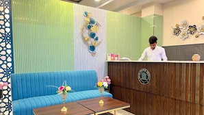 A hotel reception area with a blue sofa, a wooden reception desk, and a decorative wall with vertical stripes. - Hotel Highway Retreat (Dhanaura)