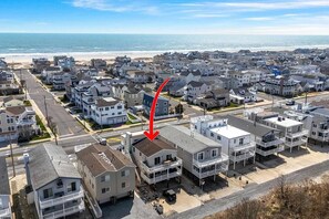 A coastal residential area with multiple two-story houses, a clear view of the beach, and a prominent red arrow pointing to a specific house.