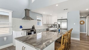 Una cocina moderna con armarios blancos, una isla grande, electrodomésticos de acero inoxidable y vistas al área de estar.
