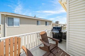 A balcony with a grill, a wooden chair, and a white railing.